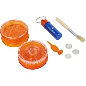 Zawartość zestawu Side Kit Storz & Bickel rozłożona na białym tle: pomarańczowy młynek, aluminiowy pojemnik z kółkiem na klucze, pędzelek, narzędzie do ubijania i trzy metalowe sitka.